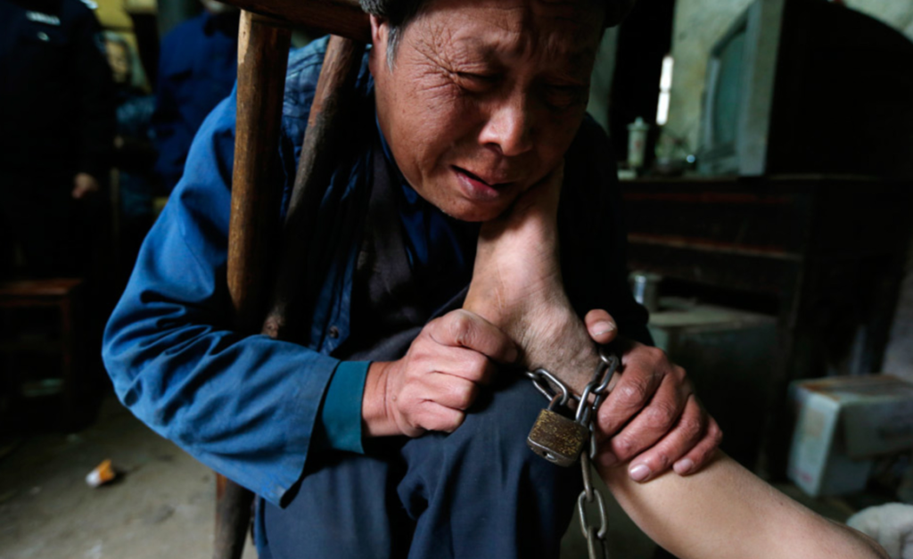 The grandfather painstakingly holds his grandson's foot, He Zili, who suffers from mental challenges. The family must physically restrain Zili because his mental state can occasionally result in violence.